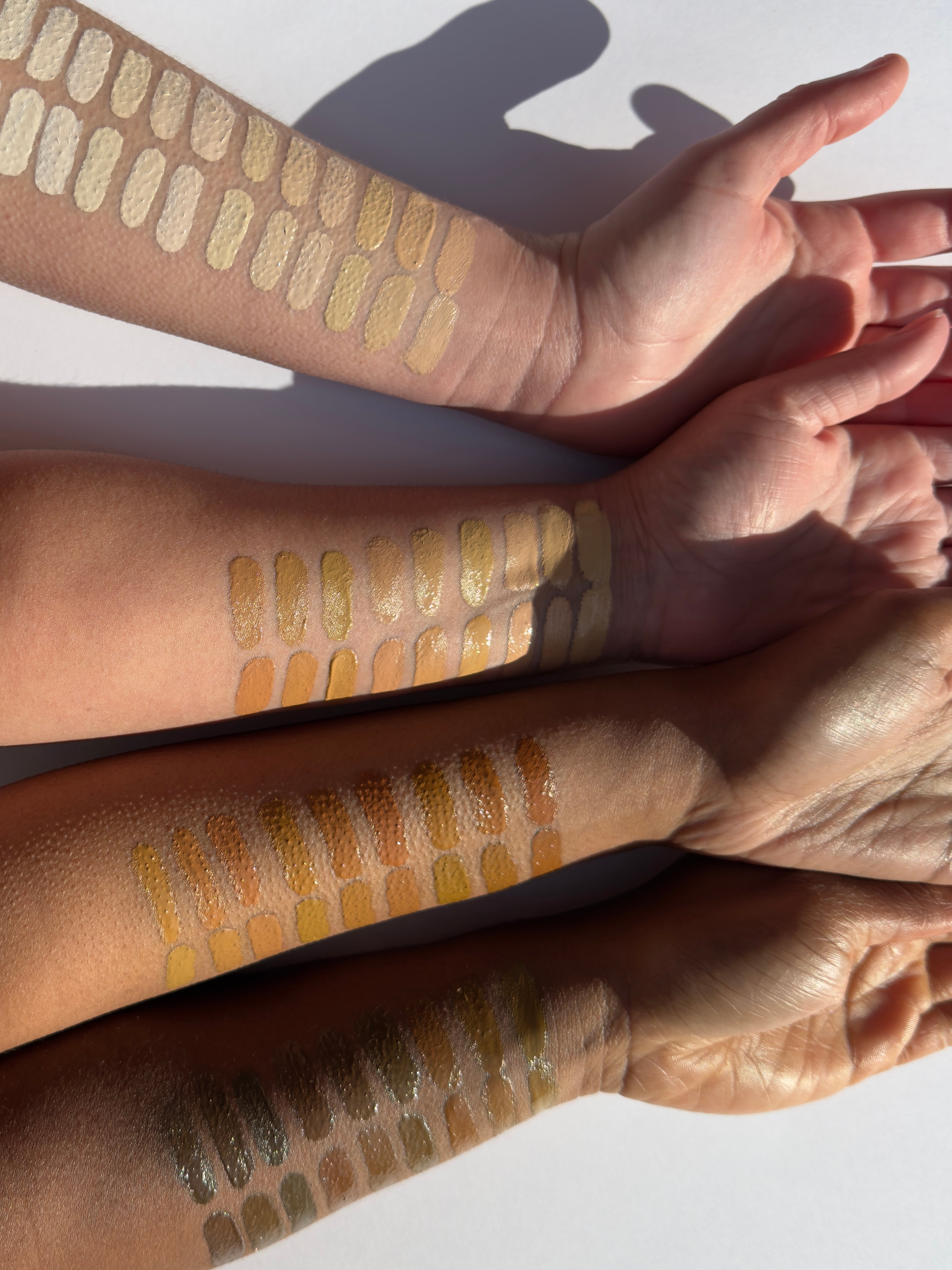 78 different foundation shades shown swatched across four arms of different skin tones from fair to deep in front of a white background in strong sunlight